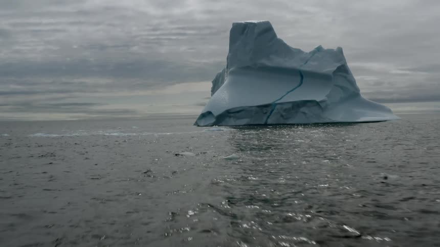 Blue iceberg with a large crack floats across ocean on an overcast day