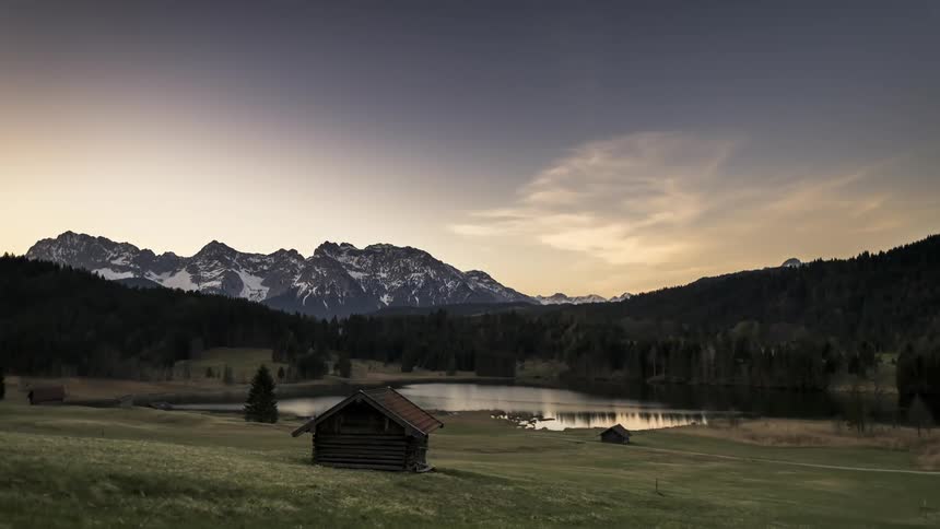 Time lapse of sunrise over a calm lake in a valley with green grassy fields