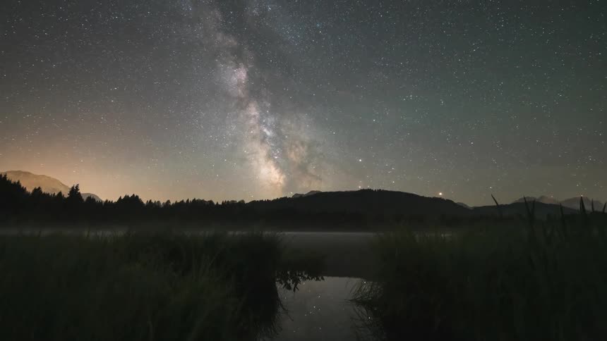 The milky way galaxy moving across a nighttime sky over mountains and a stream