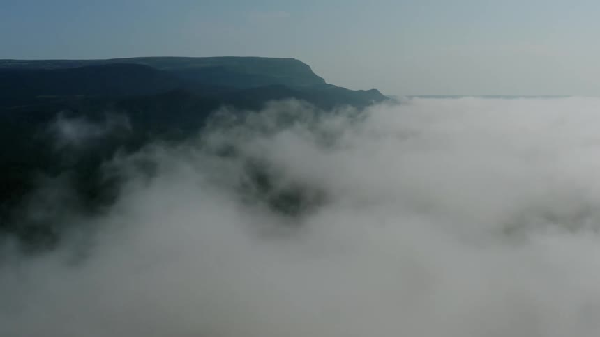A misty landscape with partially obscured mountain ranges enveloped by low lying clouds