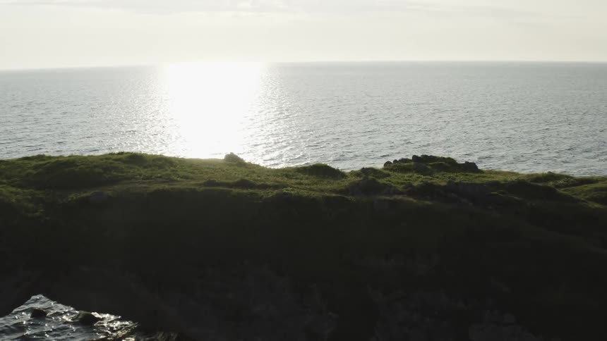 Band of ocean water reflecting the bright sunlight reaches rock formation on the shore
