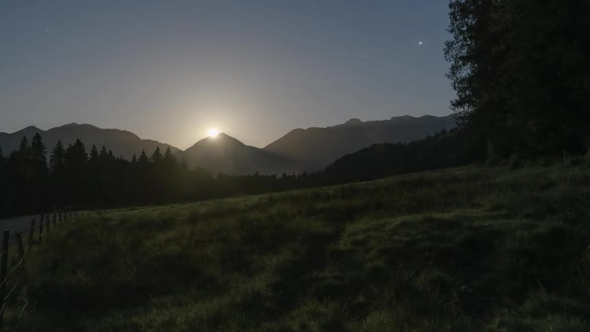 A morning with the sky shining brightly in the sky in a region with a mountain range in the background and pine trees