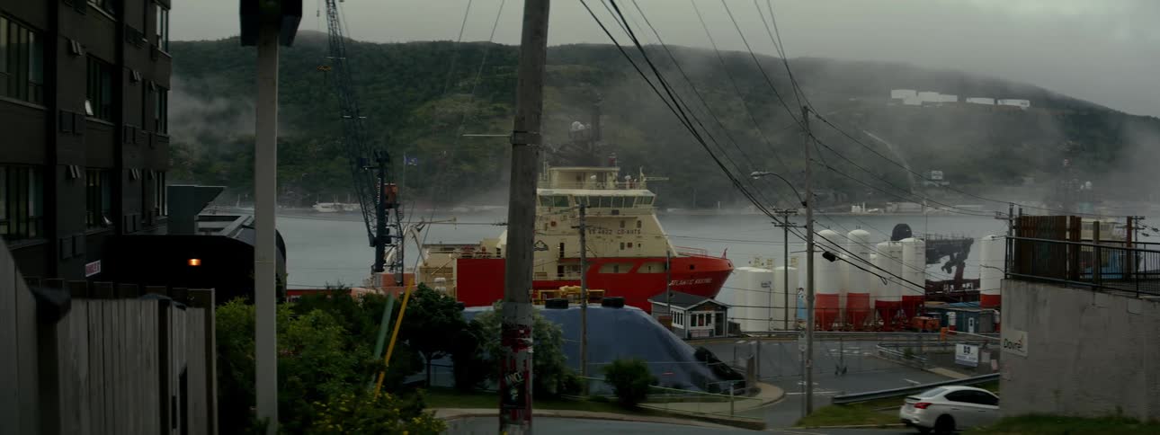 A large white and red boat moored in a port and nearby there is a street with a white car passing by