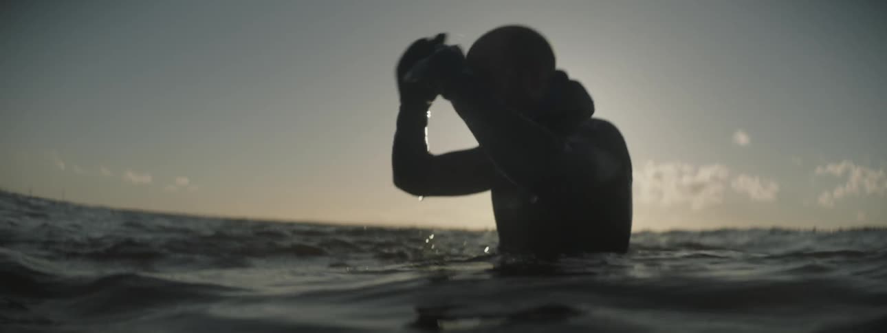 Surfer floating in swaying ocean water as sun sets
