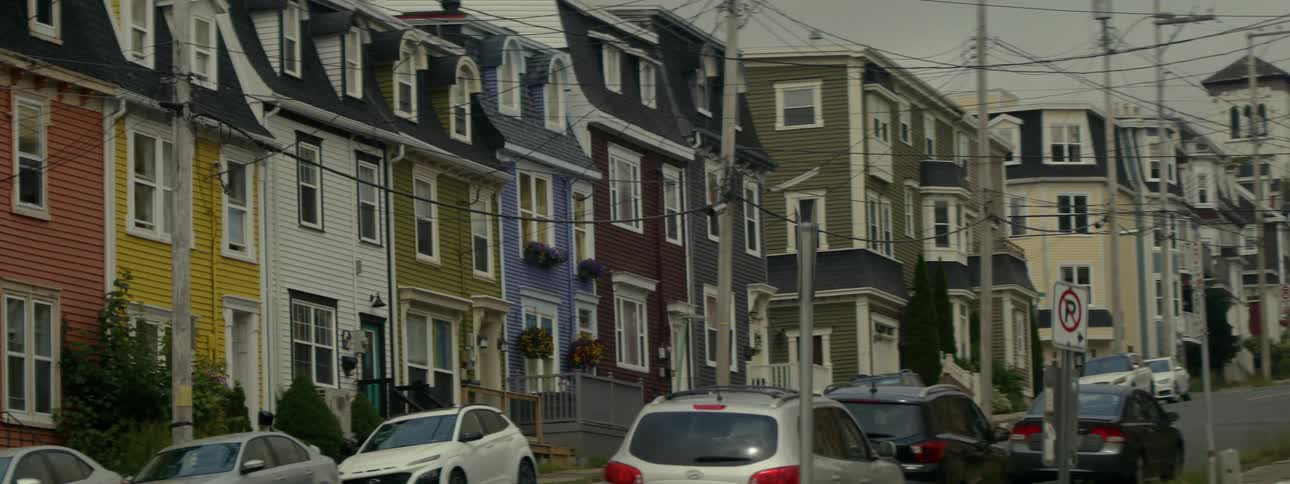 Parked cars line the street in front of row houses of different colors