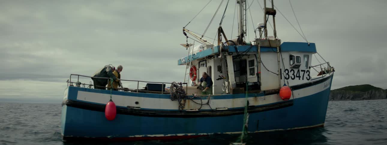 Two men work on a commercial fishing vessel near a coast