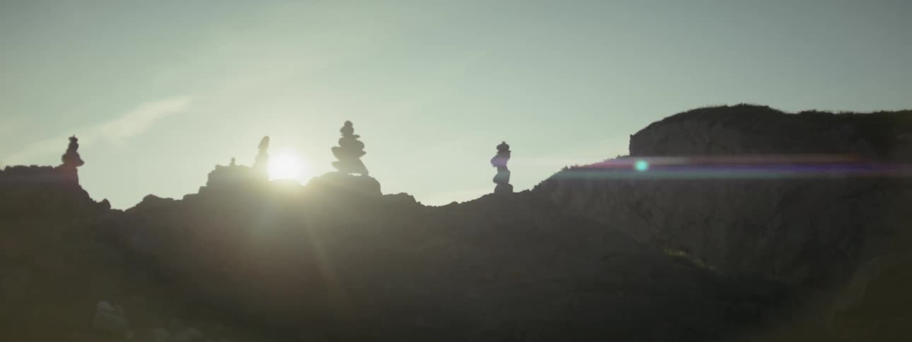 Four piles of a few small stones stacked on top of larger stones in bright sunlight