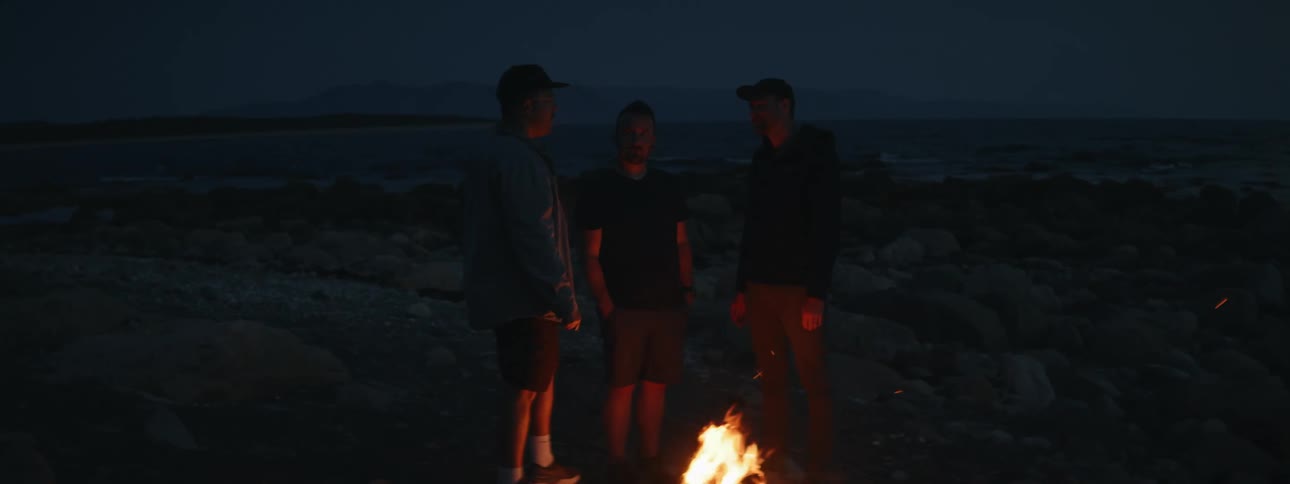 Three men around a campfire by the mountain at night