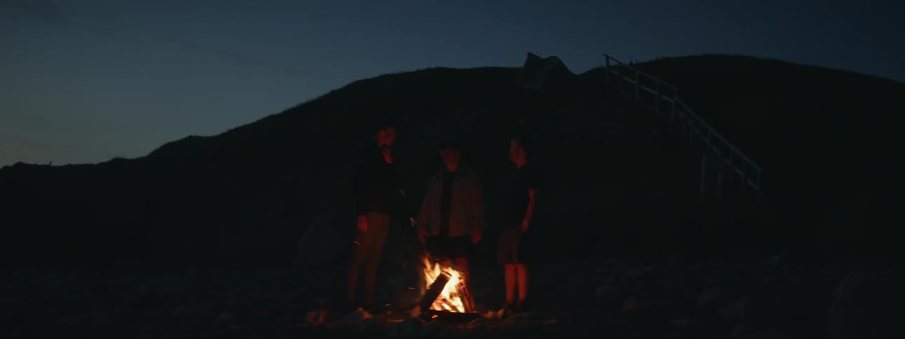 Silhouette of three people around a campfire in a natural environment at night
