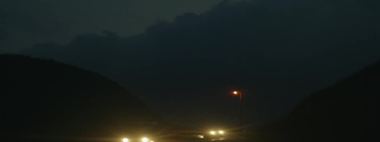 The bright headlight of a car driving down a road at night with hills on the sides