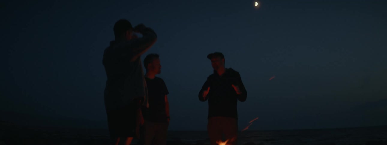 Silhouettes of three men talking around a campfire at night