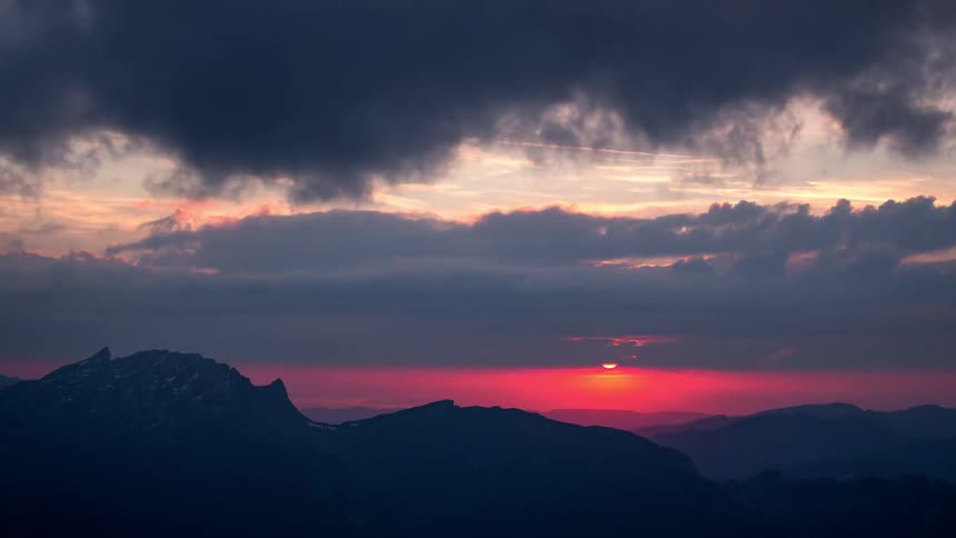 Time lapse of a sunset partially obscured by clouds over the mountains