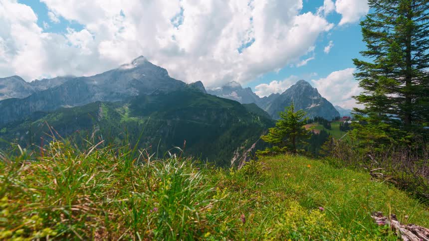 A mountainous region with lots of green grass and white clouds passing quickly in the sky
