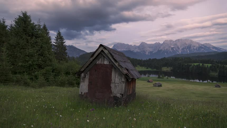 A wooden cabin in a field of grass and its getting dark quickly