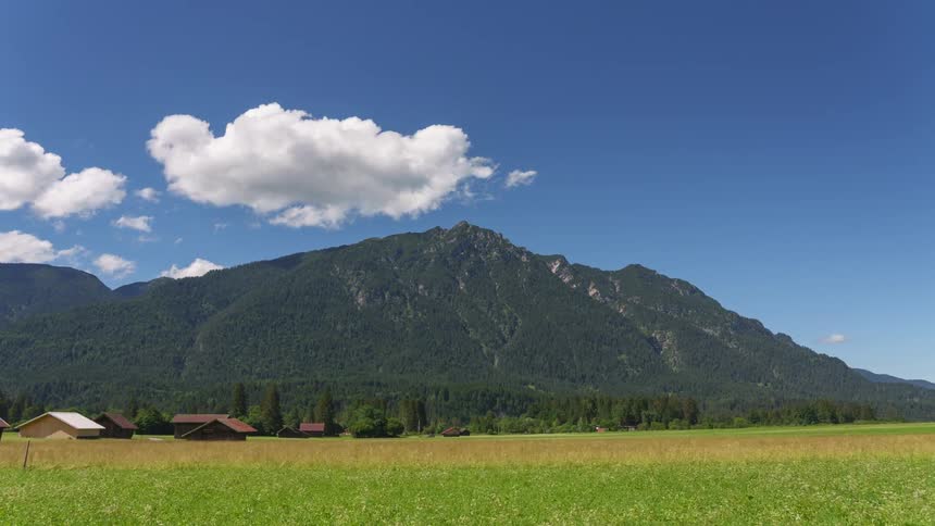 A small town in a field of green grass and a huge mountain with forests behind