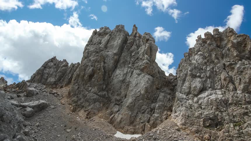 Rocky mountain ranges with erosions and clouds passing in a blue sky