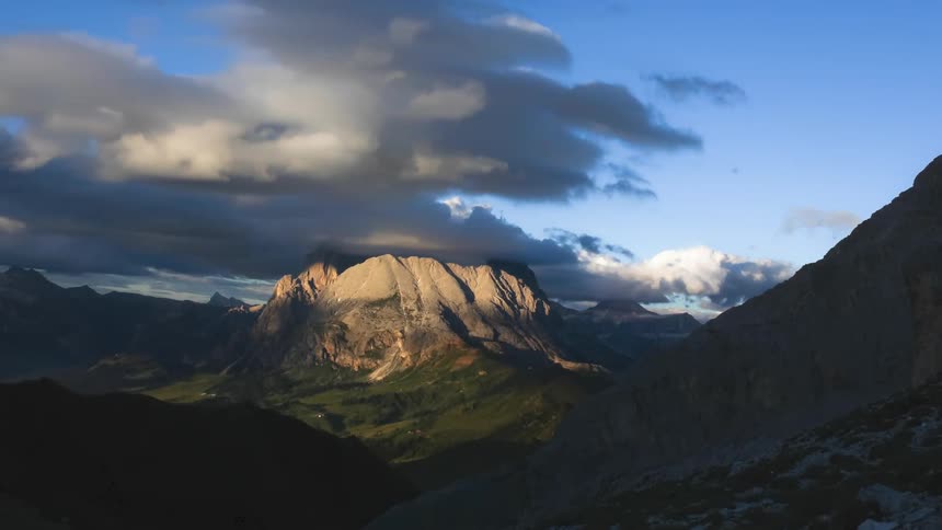 Clouds flowing across mountainous terrain cast shadows as day turns to night