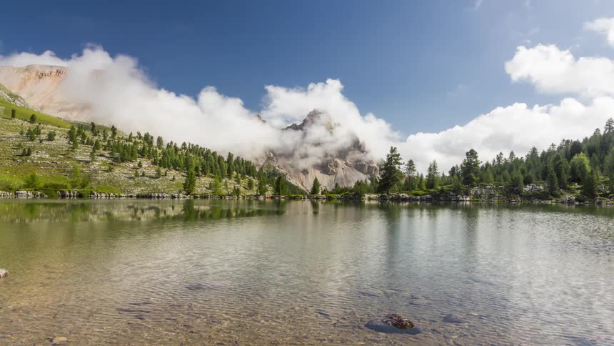 Time lapse of clouds rolling over a tranquil mountain lake surrounded by mountain peaks