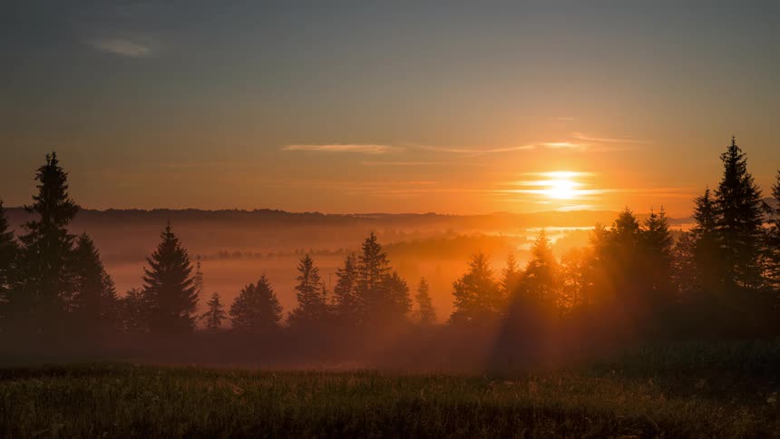 Massive fog banks fill a mountain valley as the sun rises on the horizon