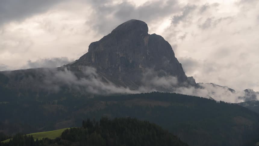 Imposing mountain with a rounded top partially hidden by low clouds under an overcast sky