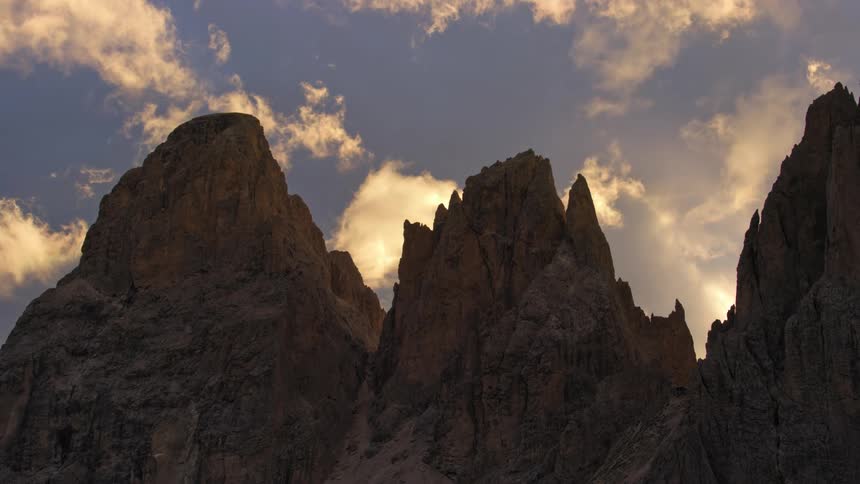 Clouds move rapidly over craggy mountains as daytime turns to dusk