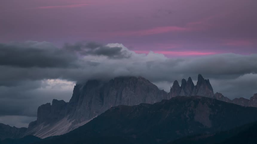 Rocky mountain ranges with cliffs and clouds passing by as the day sets in