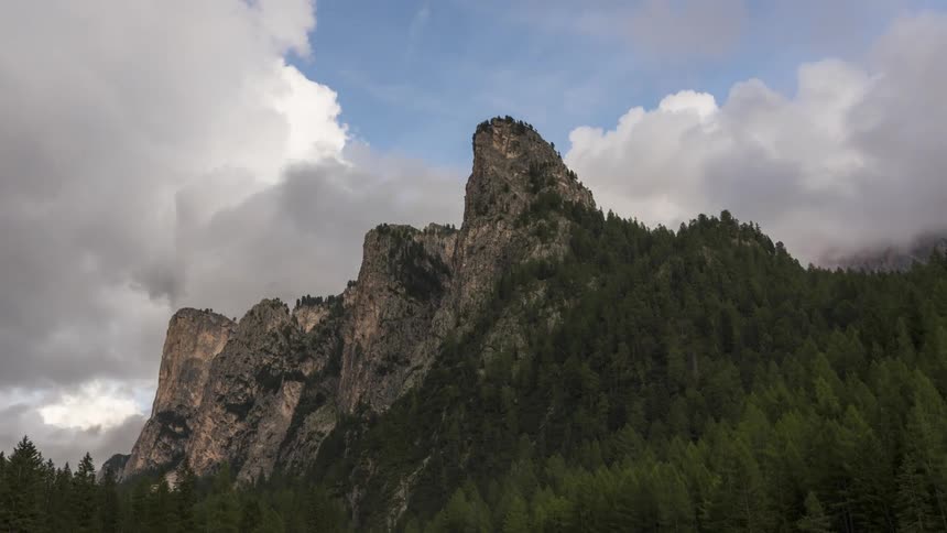 Rocky mountain range with conifers around and clouds passing by