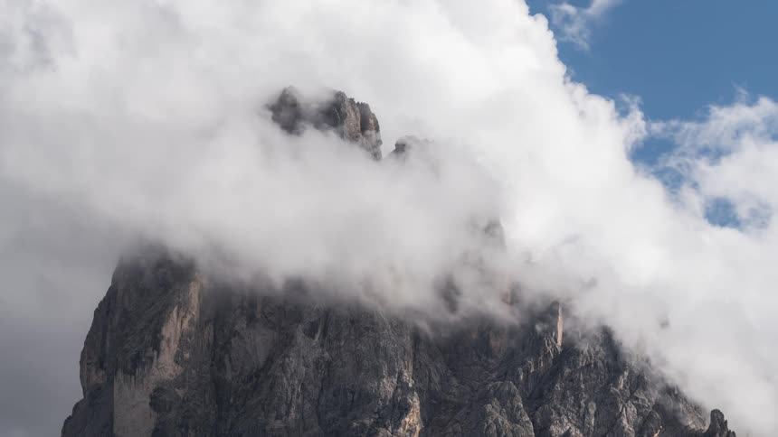 Time lapse of clouds rolling over steep mountain peaks under a blue sky