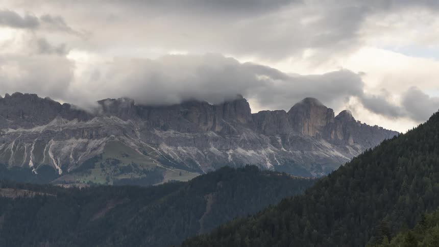 Forest covered mountains face ice streaked stone mountains on a cloudy day