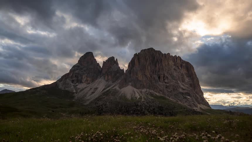 Clouds pass over jagged mountain surrounded by a field containing wildflowers