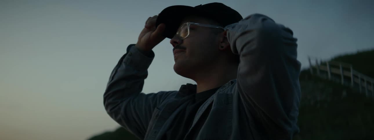 Man with glasses putting on a cap in an outdoor environment at dawn