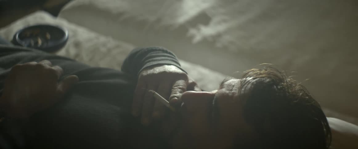 A man lies on his back smoking a cigarette in bed