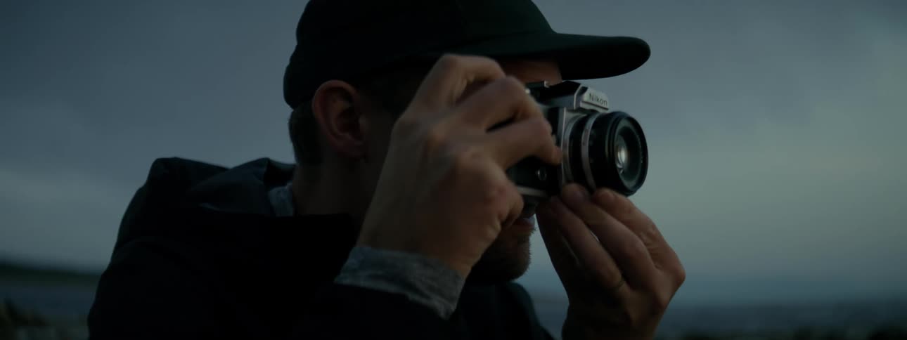 A man wearing a cap is bringing the camera to his face to take photos on a cloudy day