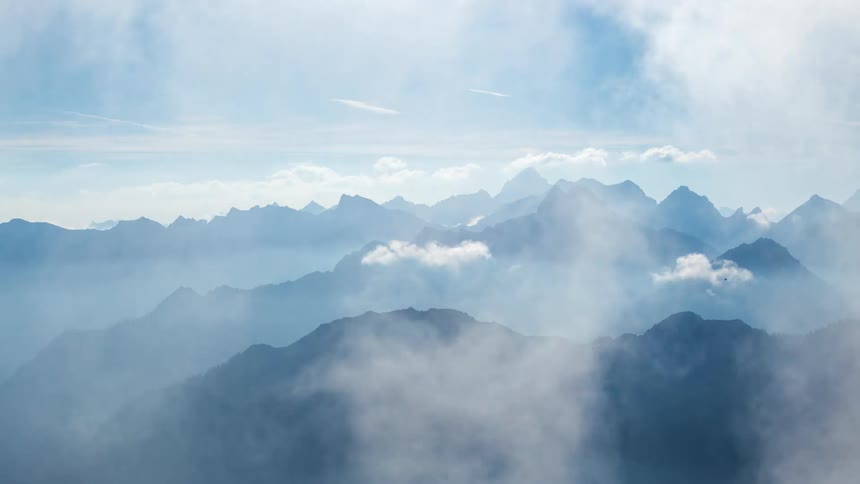 Time lapse of clouds rolling over the mountain peaks under a hazy blue sky