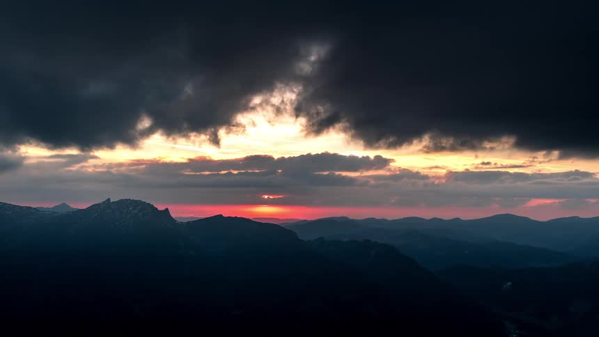 Sunset with rays of sunlight breaking through dense clouds and illuminating a mountainous terrain