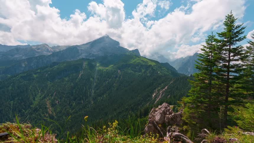 A time lapse shows clouds passing above a mountain range on a sunny day