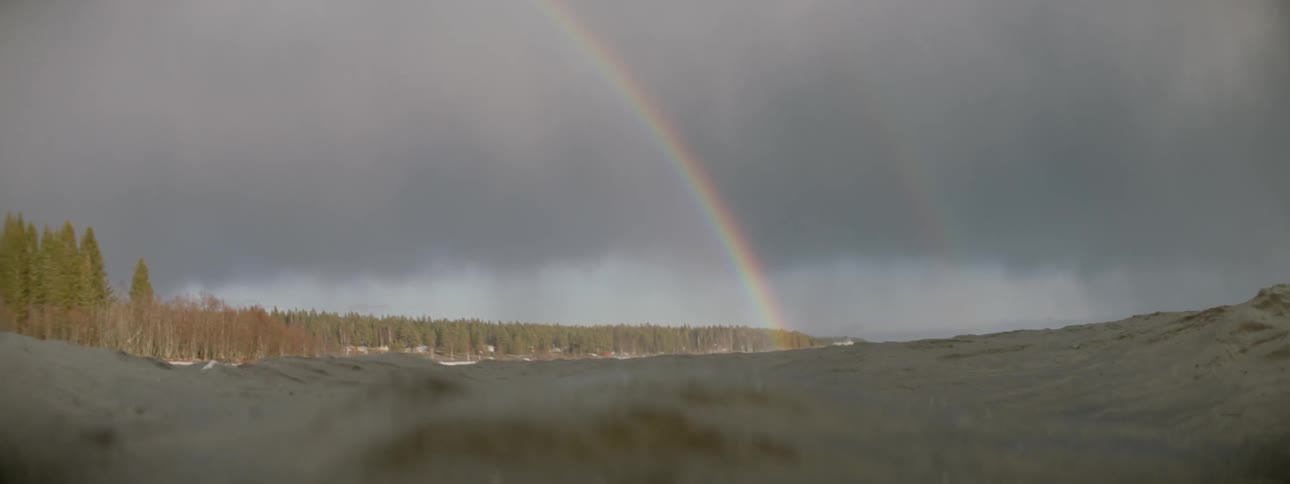As the rain splashes down in the waves, a rainbow stretches across the cloudy sky