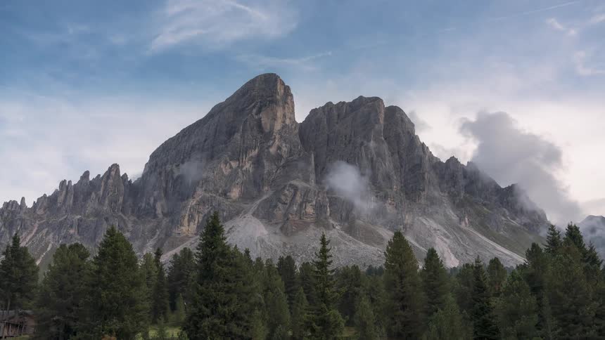 Time lapse of a majestic mountain range with a prominent peak partially shrouded by clouds