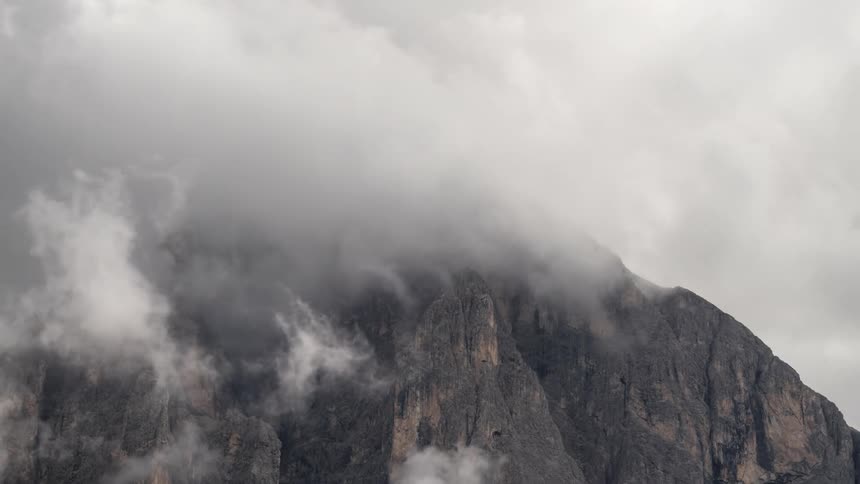 A rocky mountain stands tall and is enveloped in clouds in this time lapse