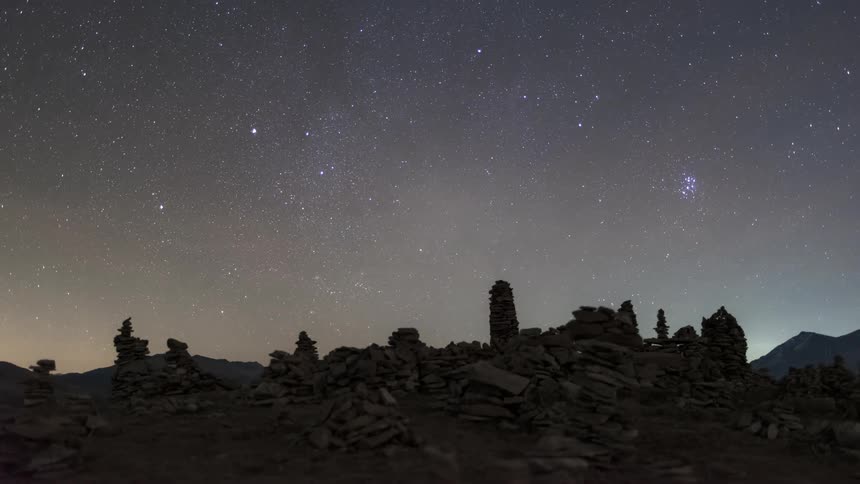 Stars and constellations march across a night sky over ancient ruins