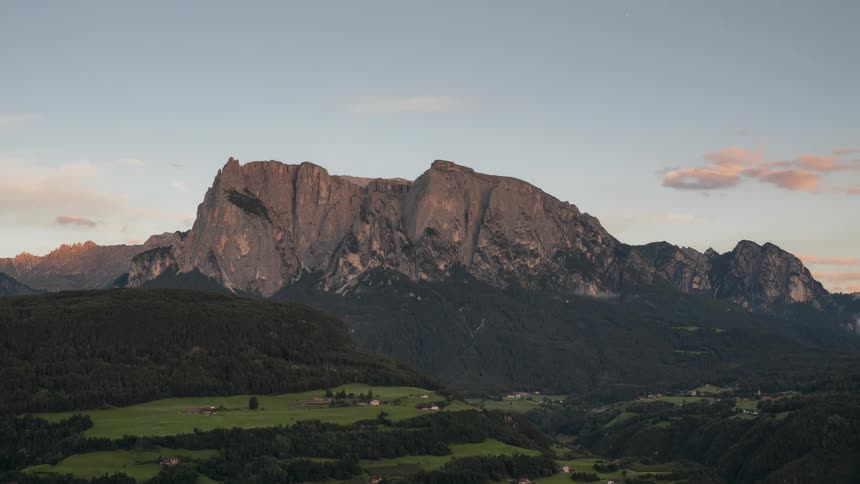 Large mountain with the top illuminated by the setting sun standing out against a clear blue sky with some darkening clouds