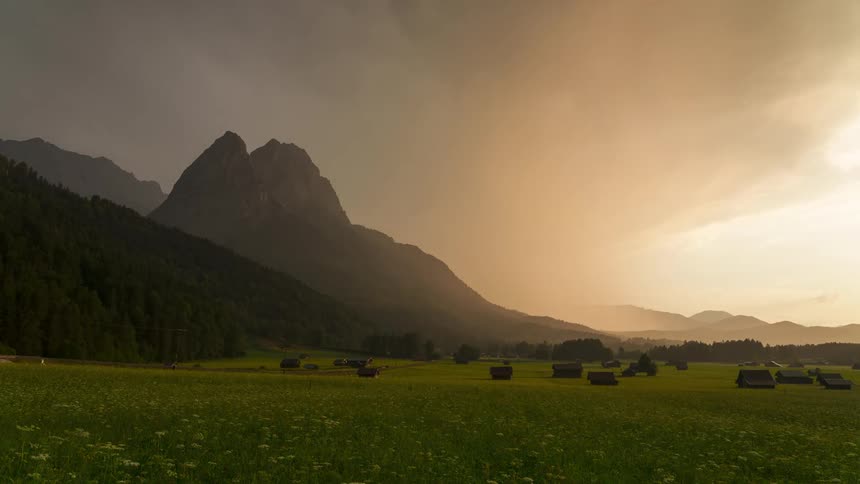 Landscape of small houses in a field surrounded by mountains and the late afternoon sky