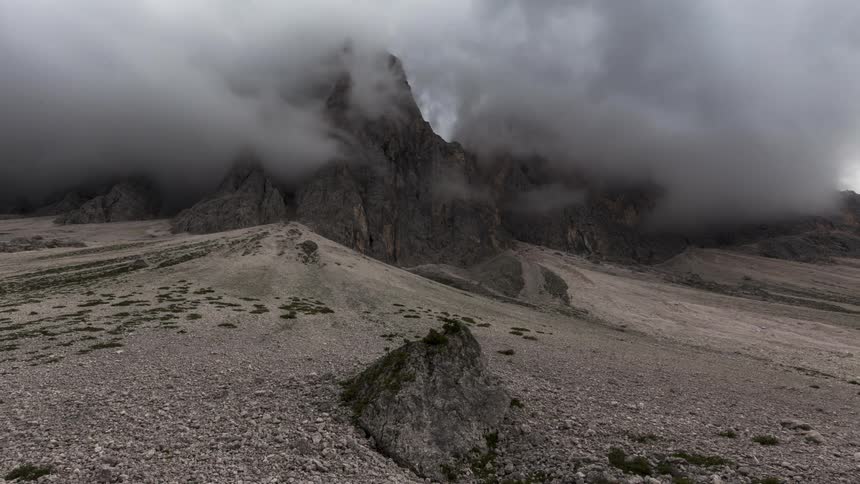 Mountainous landscape under a cloudy sky with clouds touching the peaks and a rocky terrain