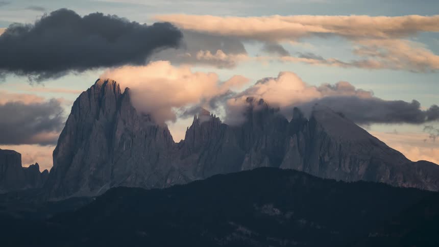 Landscape of majestic mountains with sharp peaks partially covered by clouds illuminated by the rising sun