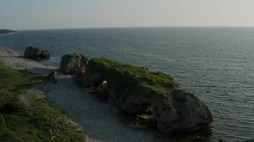 A rock formation filled with grass on top that is on a beach next to a calm se