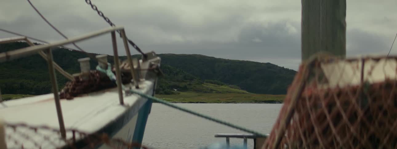 A lone seagull flies over the ocean near the deck of a boat with ropes a winch and part of a net