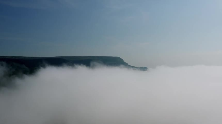 Aerial landscape above clouds and greenish mountain ranges