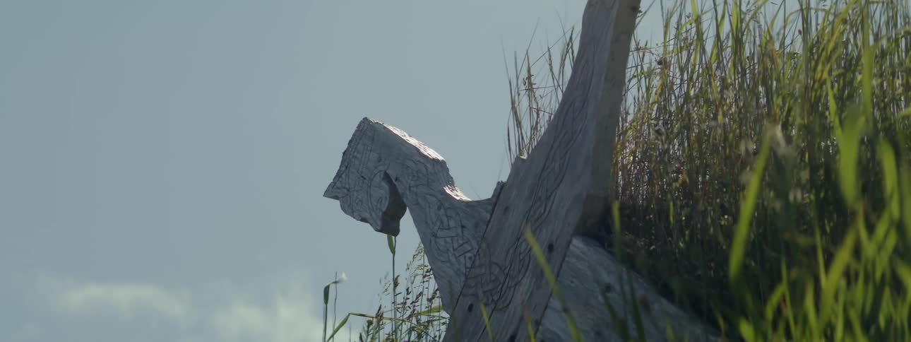 Wooden sculpture against a clear sky with some clouds and tall grasses