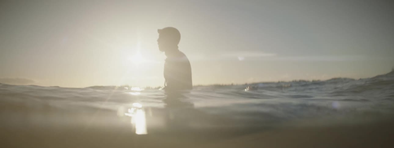 A surfer sits on his board in the ocean at sunset