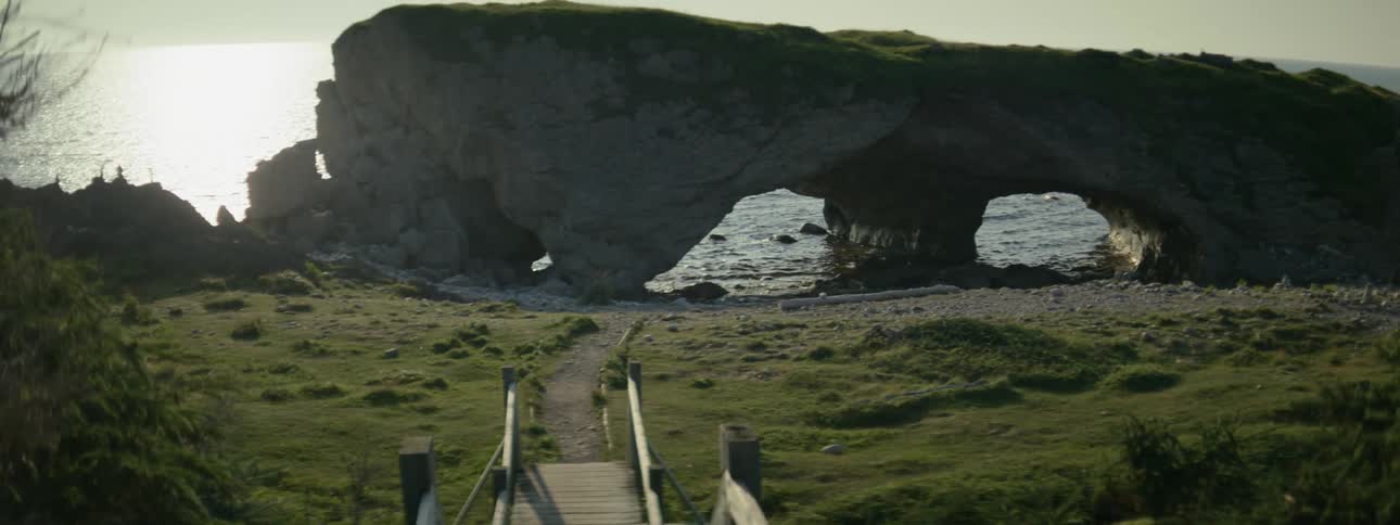 A wooden boardwalk that leads to a rock formation with holes and is partially in the sea